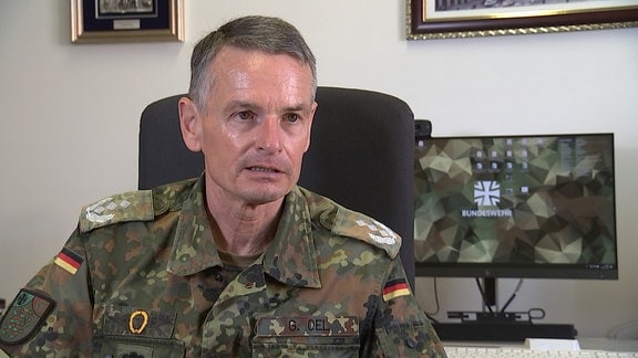 Ein älterer Mann in Bundeswehr-Uniform sitzt an einem Schreibtisch und schaut in die Kamera.