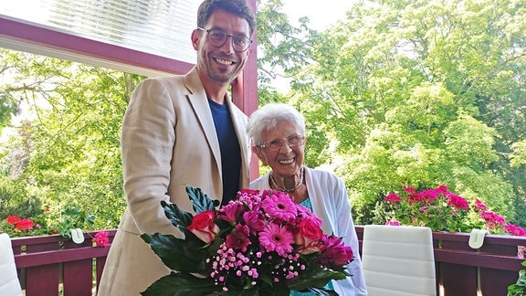 Mann mit Blumenstrauß neben Seniorin