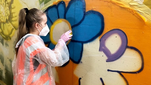 Eine Schülerin malt ein Graffiti an die Wand.