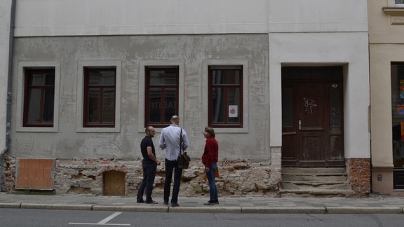 Drei Menschen stehen vor einem Haus.