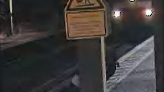 Bilder einer Überwachungskamera auf Bahnsteig, wo ein Jugendlicher einen Mann unmittelbar vor dem einfahrenden Zug rettet, dessen drei Frontlichter bereits zu sehen sind
