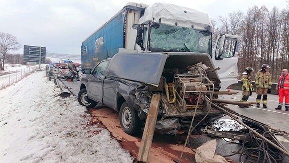 Ein Lkw ist auf der Autobahn in einen Schilderwagen gekracht. Mehrere Teile liegen heru, Feuerwehrmänner stehen am Unfallort.