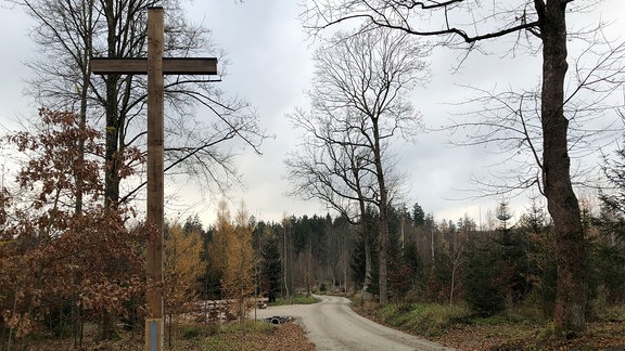 großes Holzkreuz an einem breiten Weg in Waldnähe.