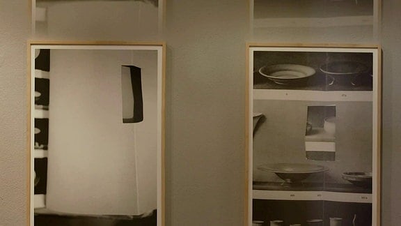 Zwei in helle Rahmen gefasste großformatige Schwarzweißfotografien hängen an einer weißen Wand.