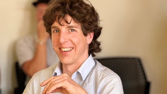 Ein Mann mit kurzem Hemd und braunen Haaren lacht