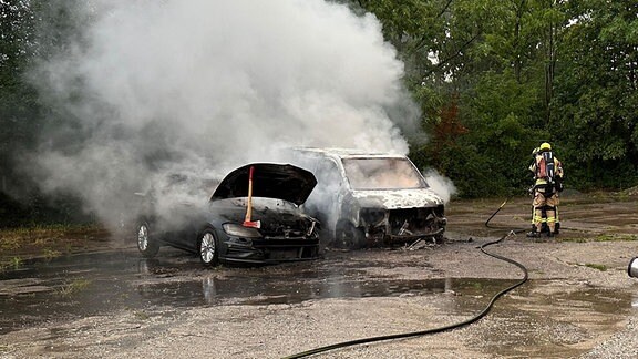 Einsatzkräfte der Feuerwehr löschen brennende Autos.