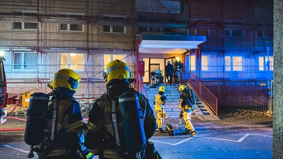 Feuerwehrleute stehen vor dem Eingang eines Hochauses.