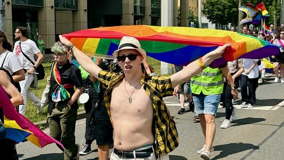 Ein junger Mann geht mit einer Regenbogenflagge bei der Demonstration durch die Straße.