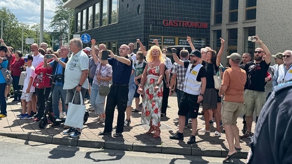 Eine Gruppe älterer Menschen protestiert gegen die Parade und streckt ihnen Mittelfinger entgegen.