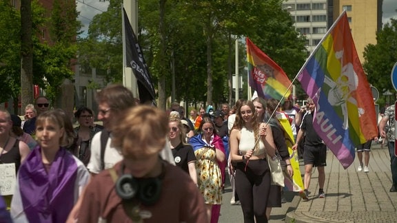 Demonstranten ziehen mit Regenbogenflaggen durch die Straße