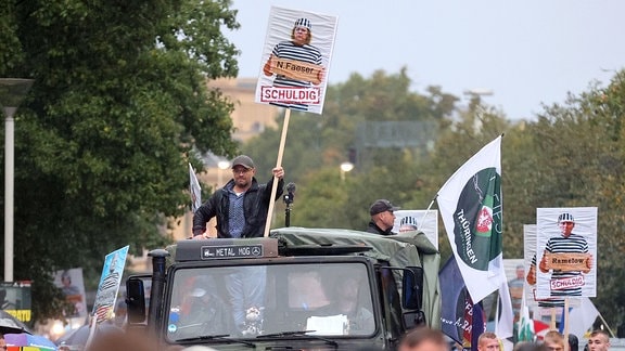 Ein Mann auf einem historischen Militärfahrzeug mit einem Plakat von Bundesinnenministerin Faeser in Sträflingskleidung.