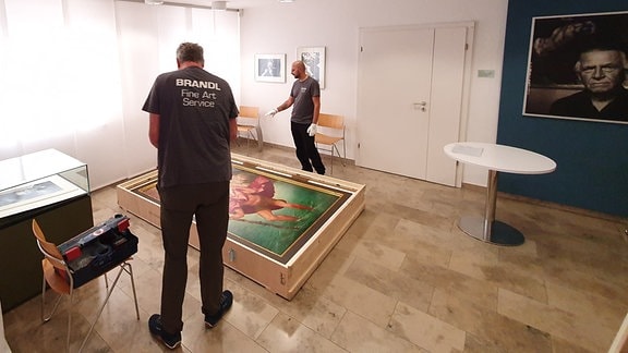 Zwei Männer neben einem Gemälde, das auf dem Boden liegt.