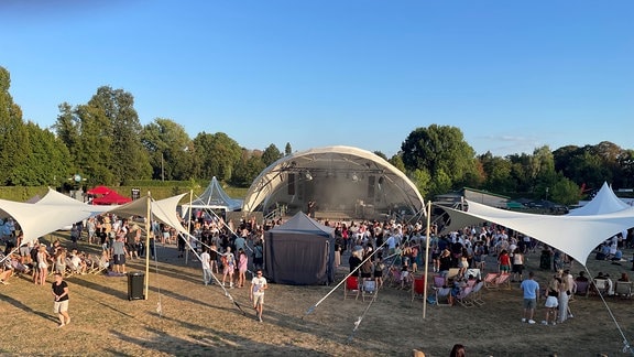 Ein Blick auf das Festival-Gelände des "Geht Raus"-Open Air in Gera. Vor einer halbmondförmig überdachten Bühne stehen, sitzen und tanzen hunderte Menschen. Links und rechts vor der Bühne sind Sonnensegel aufgespannt.