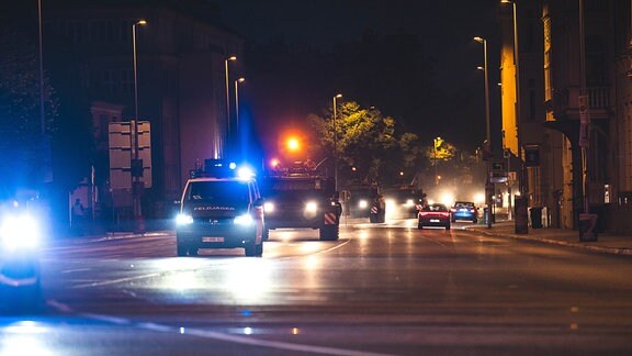 Ein Konvoi von Bundeswehr-Panzern, angeführt von einem Polizeifahrzeug, fährt im Dunkeln durch eine Straße in Gera