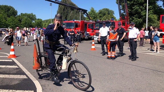 Ein Mann fährt in alter Feuerwehrkleidung auf einem Fahrrad