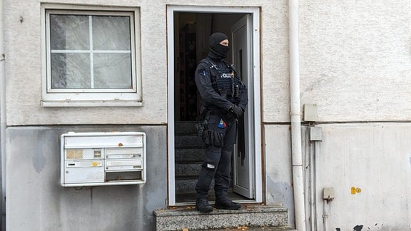 Ein Polizist steht vor einem Haus in Eisenach, das durchsucht wurde.