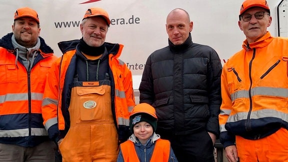 Drei Männer von der Müllabfuhr und ein Kind in Arbeitskleidung posieren mit dem Vater des Kindes für ein Gruppenfoto.