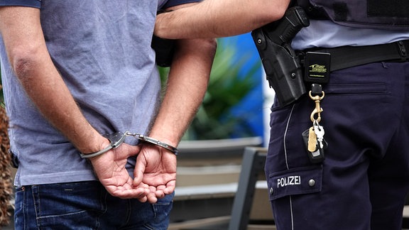 Ein Mann steht in Handschellen neben einem Polizisten