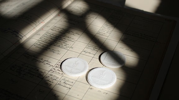 drei weiße Münzen liegen auf einem Tisch, das Fenster wirft starke Schatten.