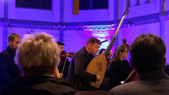 Ein Mann spielt in einem Orchester eine große Laute vor Publikum