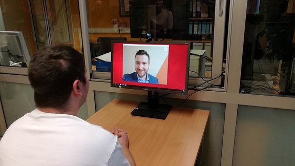 Ein Mann schaut in einen Computerbildschirm und Videotelefoniert via Skype mit einem anderen Mann