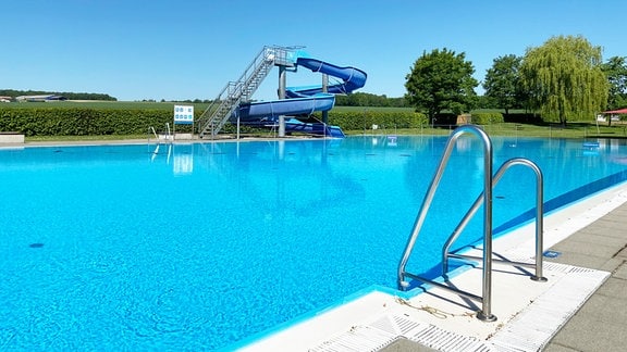 Becken eines Freibads mit einer blauen Rutsche im Hintergrund.