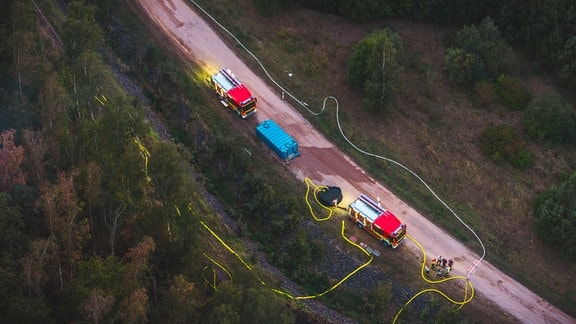  Einsatzwagen der Feuerwehr stehen auf einem Feldweg nahe eines Wald- und Wiesenbrandes.