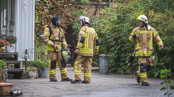 Drei Feuerwehrleute auf einem Grundstück.