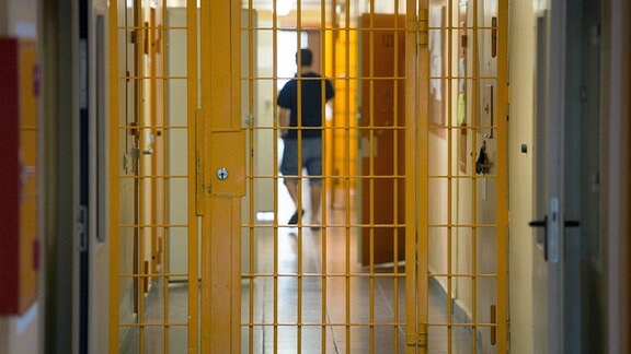 Ein Mann geht in der Justizvollzugsanstalt Hohenleuben hinter einer verschlossenen Gittertür einen Gang entlang.