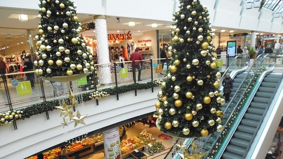 In einem Shopping-Center in Greiz mit mehreren Geschäften hängt noch vor dem Advent weihnachtliche Dekoration mit geschmückten Weihnachtsbäumen, die über einer Rolltreppe hängen