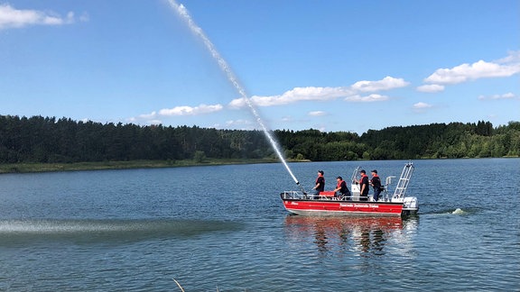 Auf einem Boot der Freiwilligen  Feuerwehr Zeulenroda vom Typ RTB2 stehen Feuerwehrleute, sie schießen einen Wasserstrahl über die Talsperre.