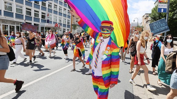 Ein Mann in regenbogenfarbener Kleidung schwingt eine passende Fahne auf dem Ernst Abbe Platz