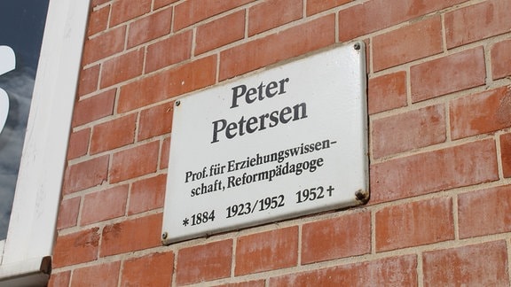 Auf einer Mauer ist ein Schild mit dem Informationen zu Peter Jansen angebracht.
