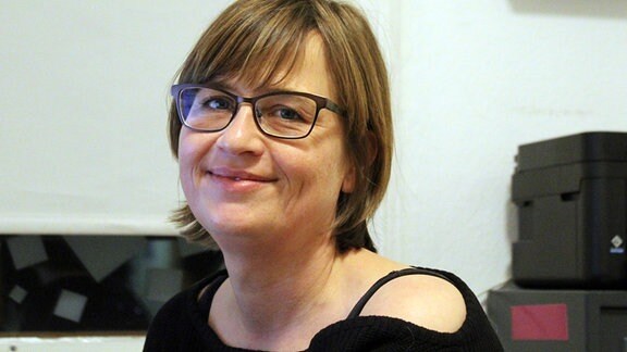 Die Teamleiterin, eine Frau mit Brille und schwarzem Pulli im Porträt, an ihrem Schreibtisch