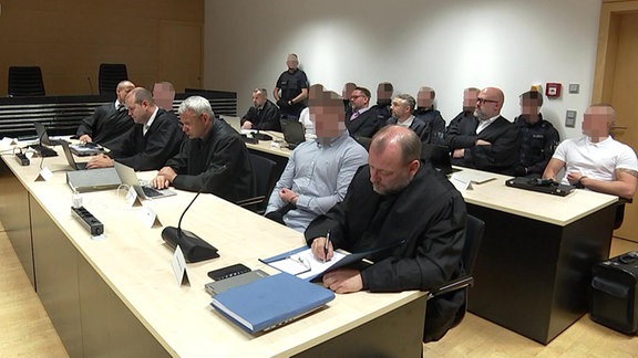 Mehrere Angeklagte sitzen mit ihren Anwälten in einem Gerichtssaal