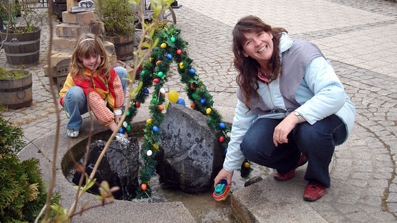 Frau und Kind haben spaß an einem mit Ostereiern geschmücktem Brunnen.