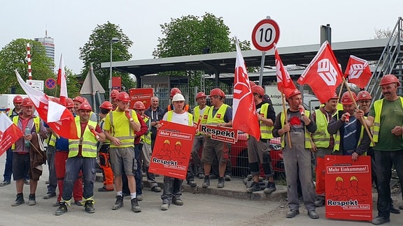 Bauarbeiter protestieren auf einer Baustelle mit Fahnen und Plakaten für mehr Einkommen.