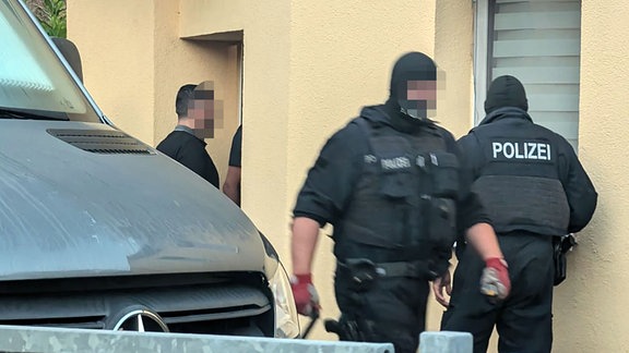 In schwarz gekleidete Polizisten stehen vor einer Hauswand.