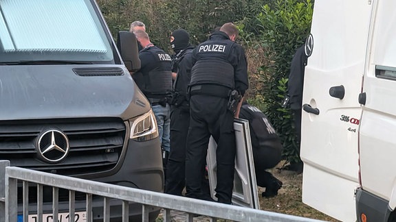 In schwarz gekleidete Polizisten stehen vor einer Hauswand.