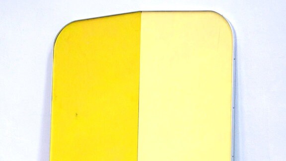 Eine an eine Wand gelehnte gelbe Skulptur von Christian Henkel, die abstrahiert eine Perücke (englisch "wig") sein könnte.