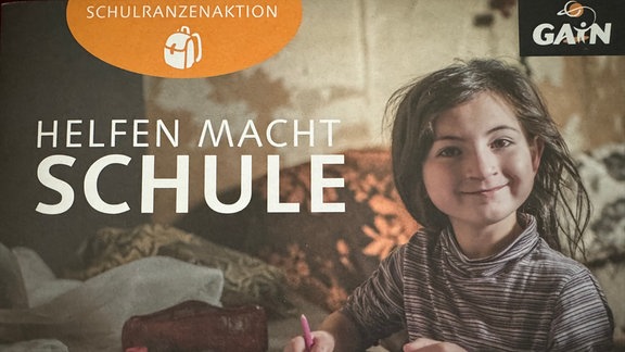 Ein Mädchen lächelt auf einem Plakat in die Kamera. Daneben ist geschrieben "Schulranzenaktion - Helfen macht Schule"