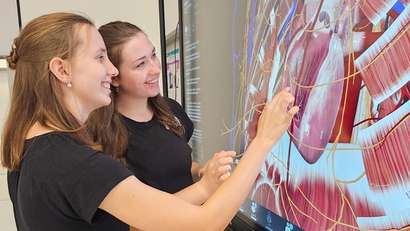 Zwei Studentinnen schauen auf einen Touchscreen mit der Anatomie des Menschen