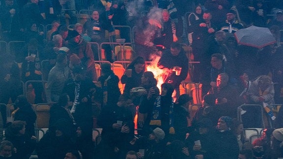 Brennende Pyrotechnik zwischen Zuschauern in einem Stadion.