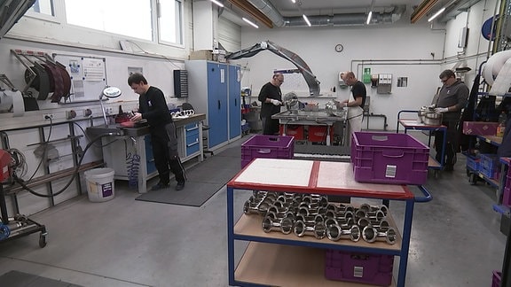 Drei Personen arbeiten in einer Produktionhalle