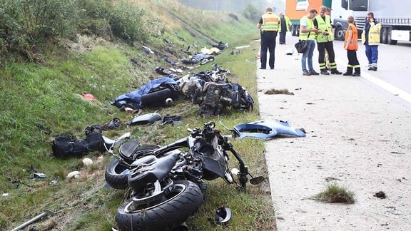 Einsatzkräfte stehen an einer Unfallstelle auf der A 9, Motorräder und Trümmerteile liegen neben der Fahrbahn an der Böschung, 2019.