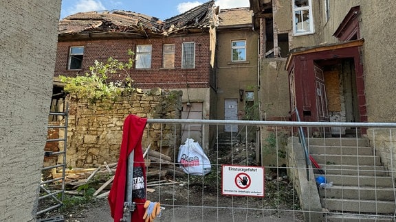 Ein Bauzaun steht vor einem zerfallenem Gebäude.