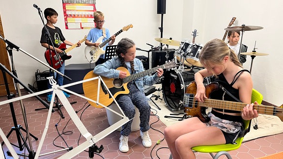 Verschiedene Schüler sitzen in einem Proberaum zusammen und spielen Instrumente.