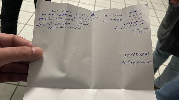 Ein Mann zeigt einen Zettel mit arabischer Schrift.