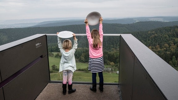 Zwei Kinder werfen Porzellanteller vom Steg der Wünsche auf der Leuchtenburg.