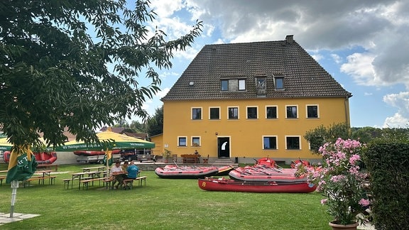 Rotes Kanus liegen auf einer Wiese, im Hintergrund ein Haus.